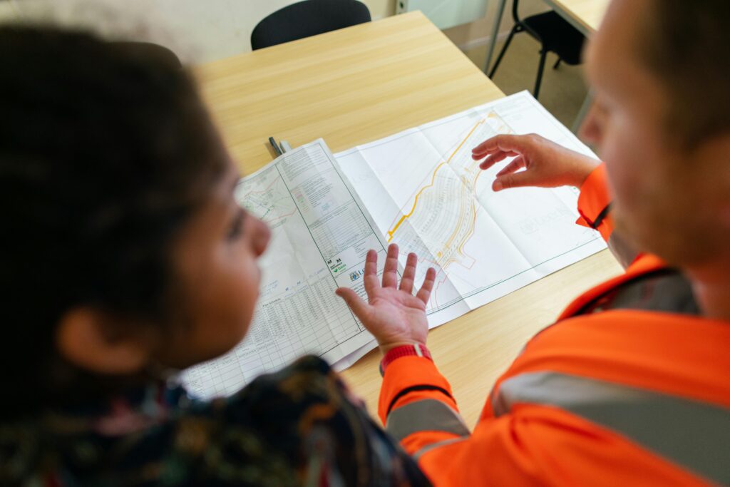 services-2 Two engineers reviewing construction blueprints on a table in an office setting.