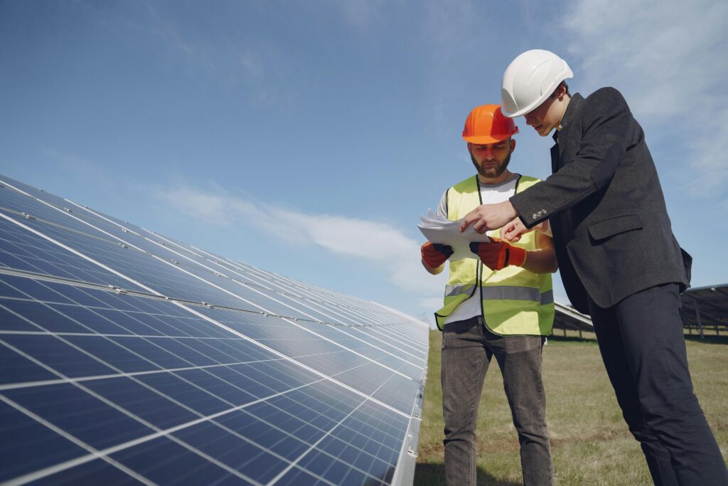 services-1 Low angle of young inspector and foreman in hardhats checking documentation against modern solar panels in field